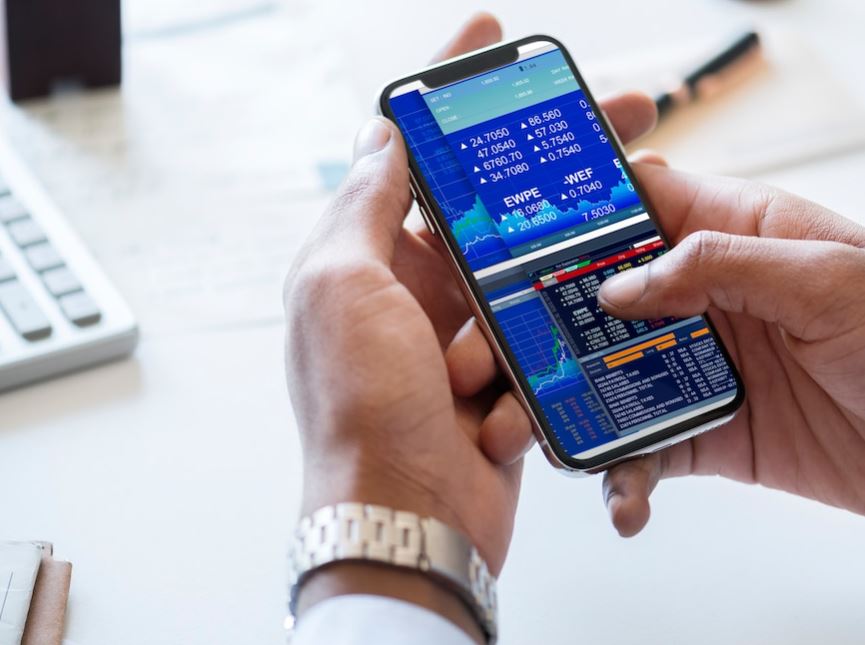 Aktien von Glücksspielkonzernen – ist ein Investment lohnenswert? Eine Person zeigt auf Aktienverläufe, die auf einem Smartphone und einem Laptop abgebildet sind